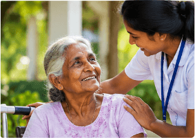 A CareBridge Lanka care coordinator smiling warmly with an elderly woman in a wheelchair