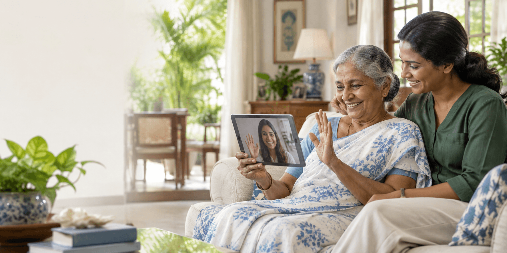 An older Sri Lankan mother smiling on a video call with her daughter while a local care coordinator sits beside her